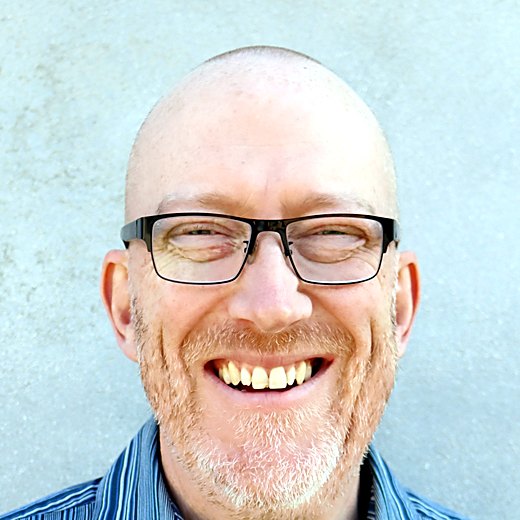 Paul M. O’Neill, smiling, wearing glasses and a blue striped shirt